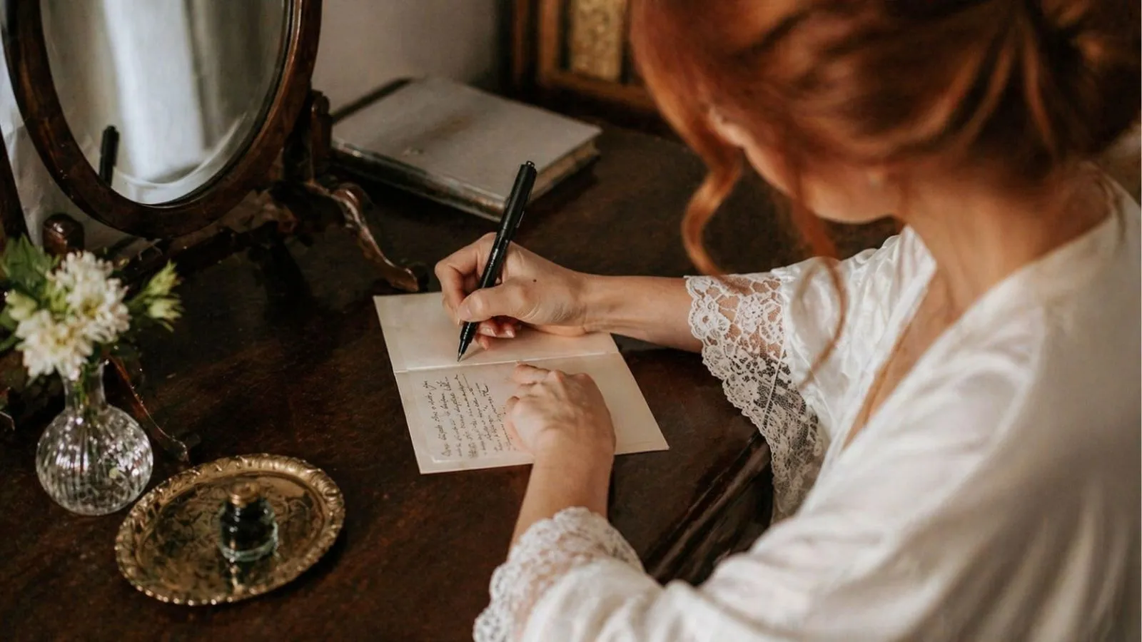 Bride writing wedding vows at a vintage desk with soft lighting