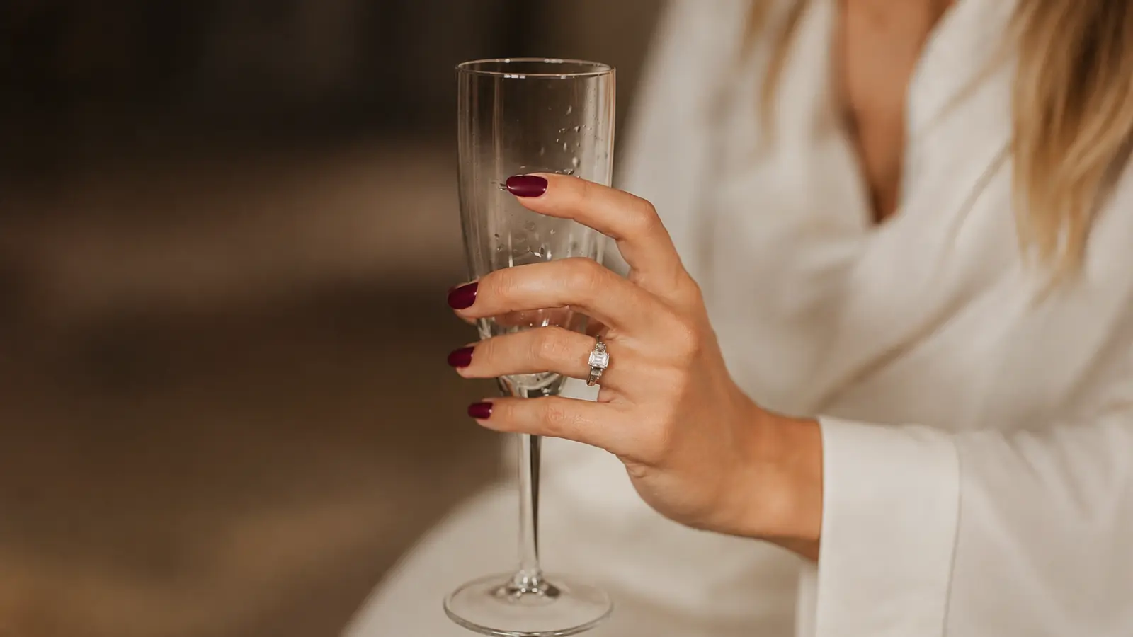 Burgundy wedding guest nails holding a champagne glass at an elegant evening event