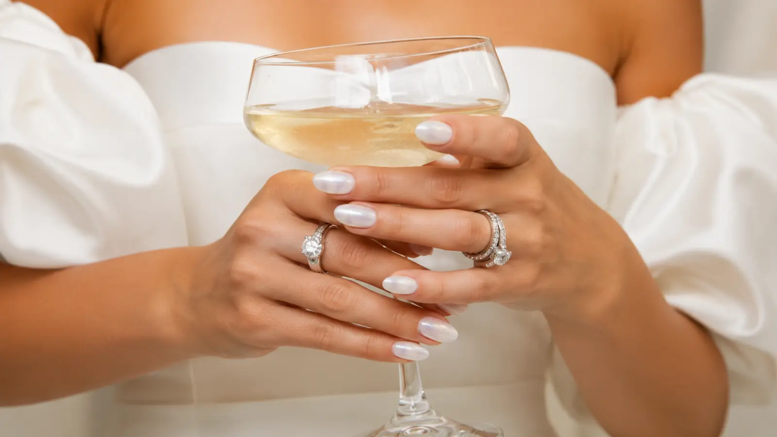 Bride holding a champagne glass with pearl white wedding nails and diamond rings