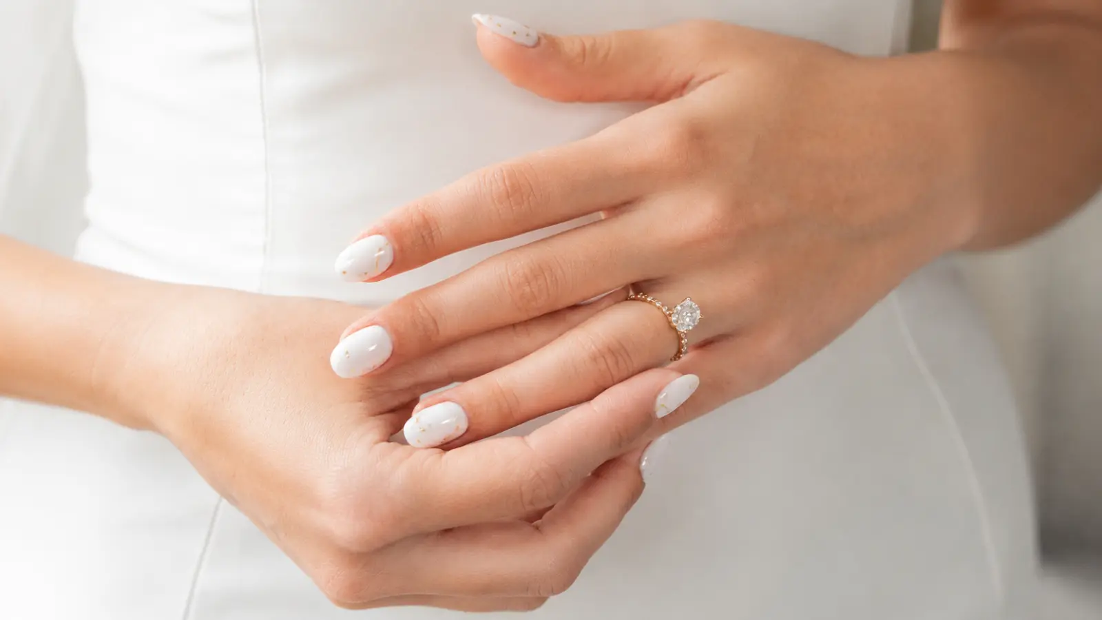 White wedding nails with delicate gold accents and engagement ring
