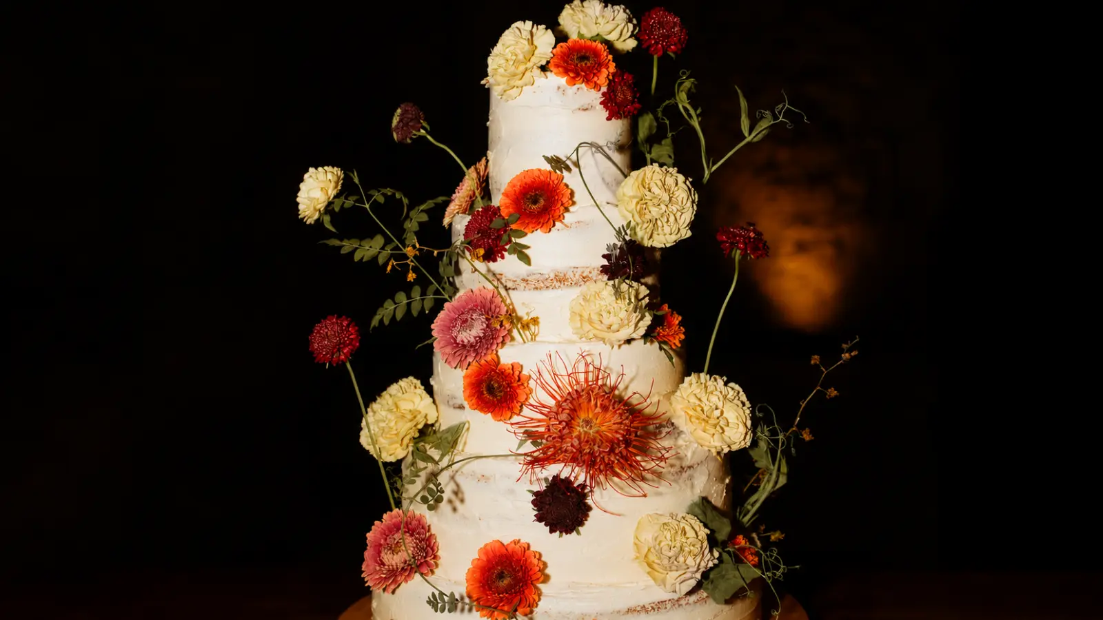 Tall autumn wedding cake with multiple tiers, colorful fall flowers, warm seasonal tones, and elegant floral decoration for a wedding reception.
