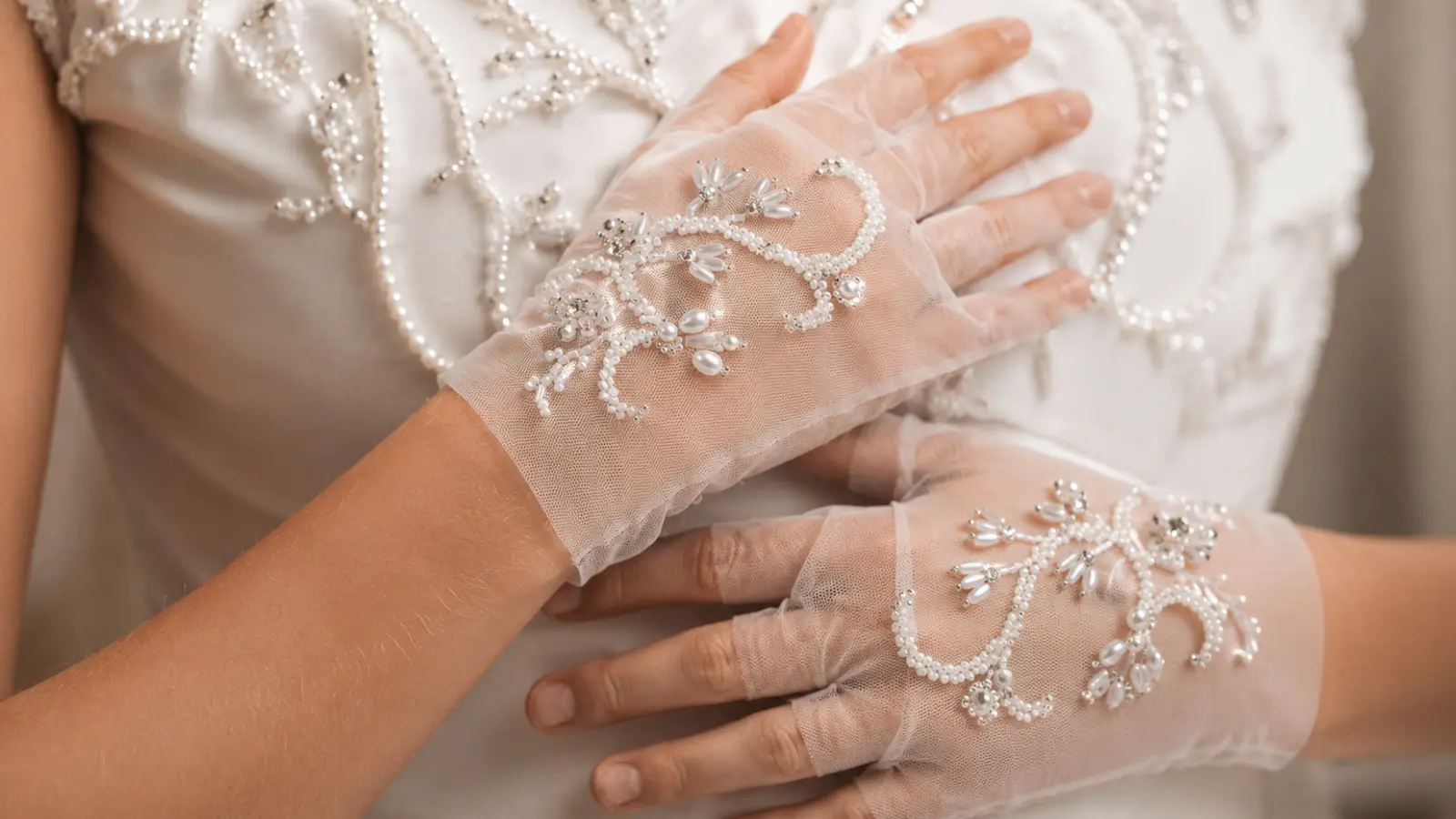 Detailed view of beaded fingerless bridal gloves with pearls and embroidery paired with an elegant wedding dress
