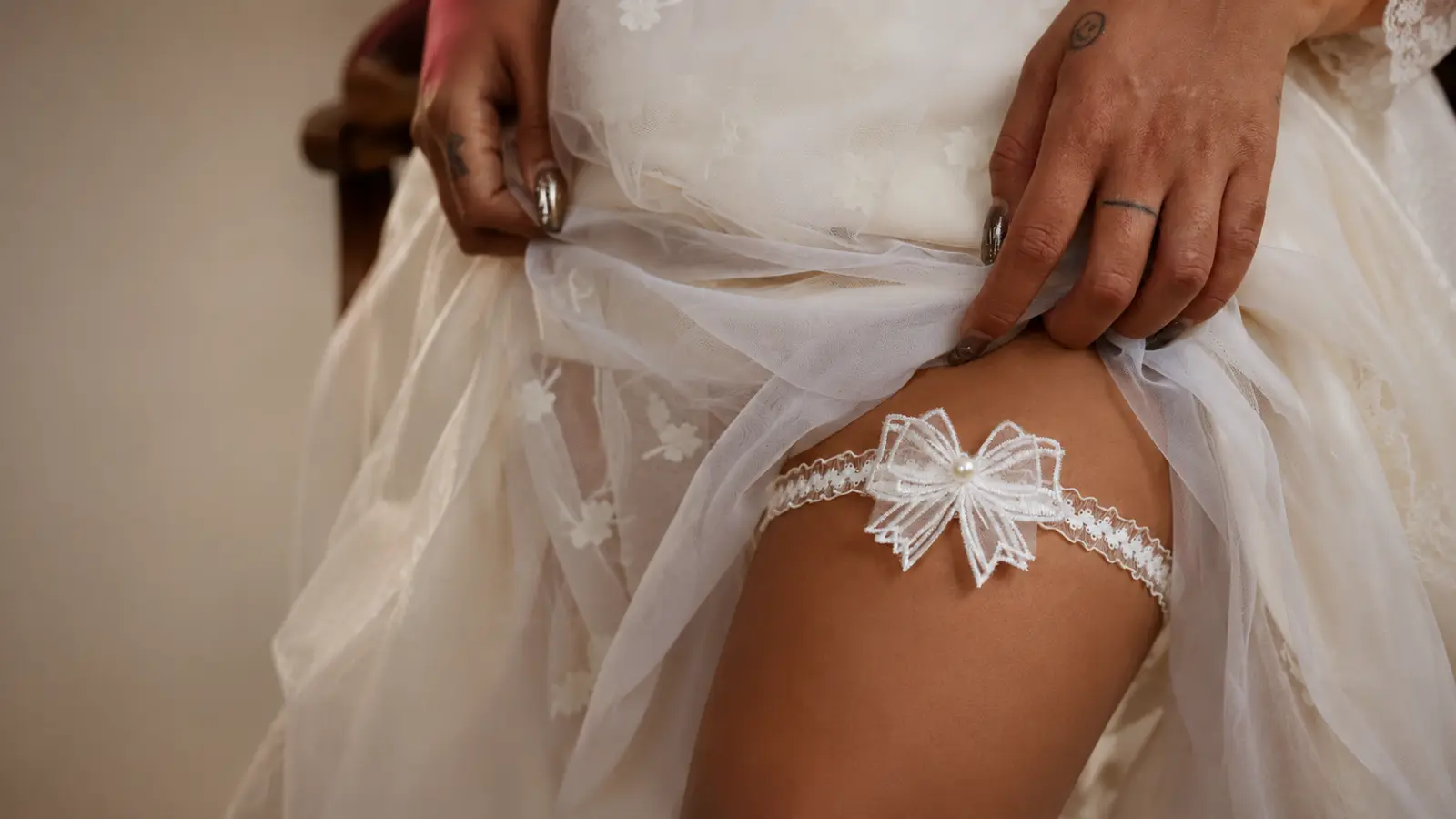 Detailed view of a lace wedding garter with a decorative bow and pearl accent worn under a bridal dress