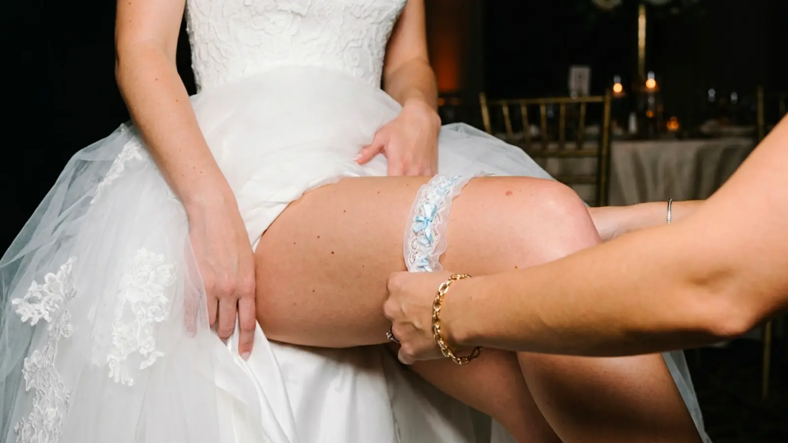 Bride trying on a blue lace wedding garter with assistance to achieve the perfect fit