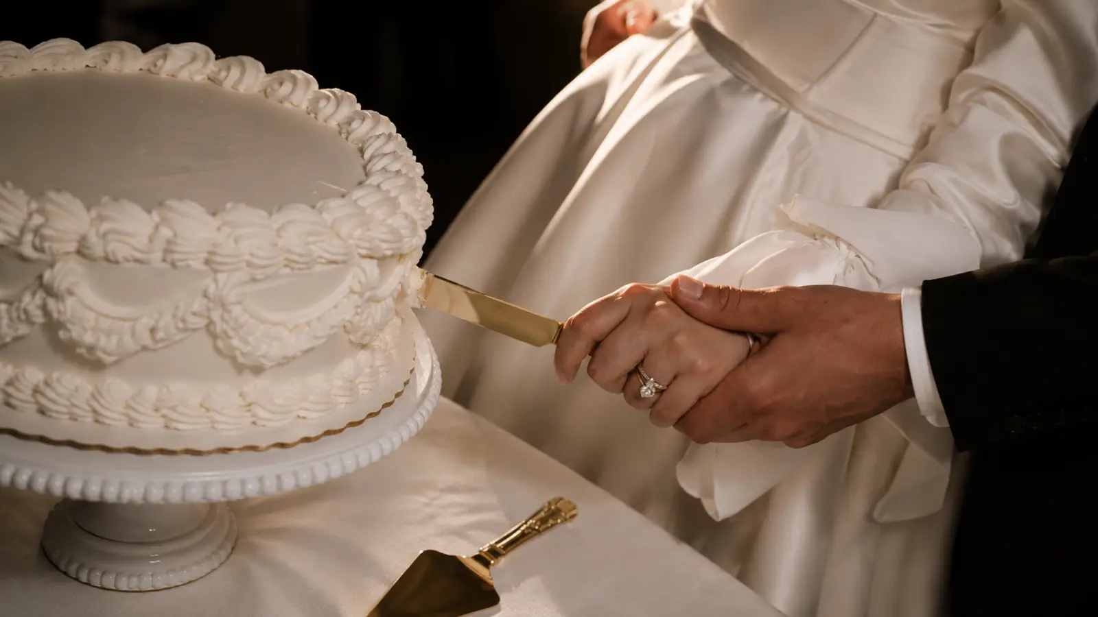 Close-up of bride and groom hands cutting a wedding cake together