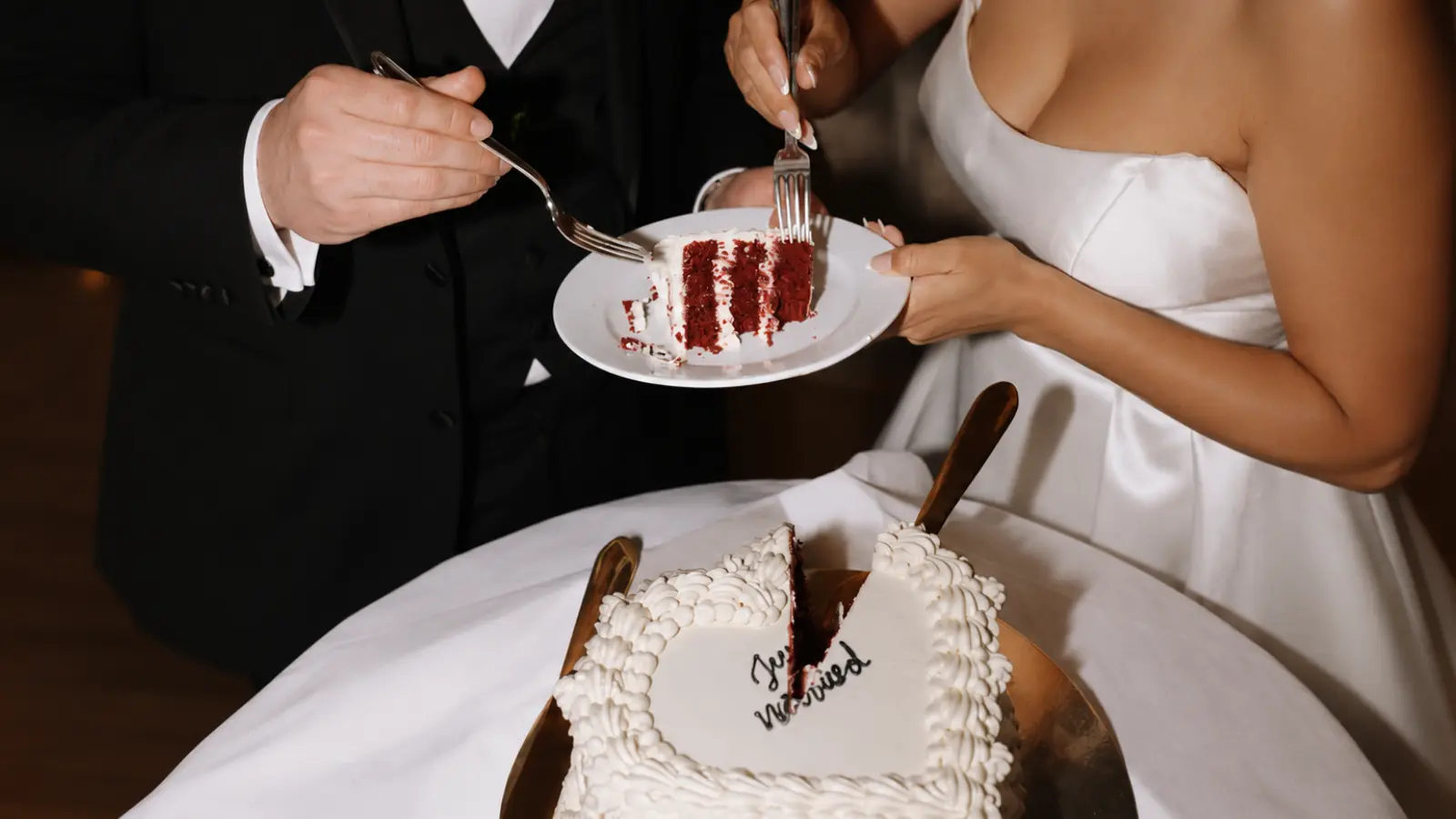 Bride and groom sharing the first slice of red velvet wedding cake cutting the cake during their wedding reception celebration.