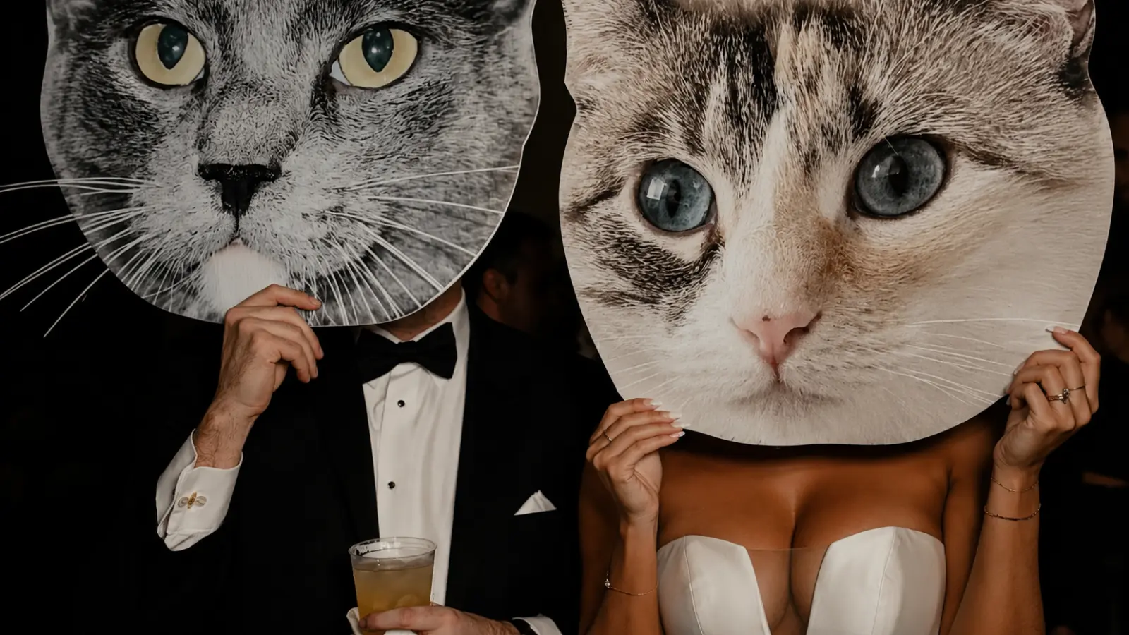 Bride and groom posing with oversized cat face photo booth props during the wedding reception to honor their beloved cats