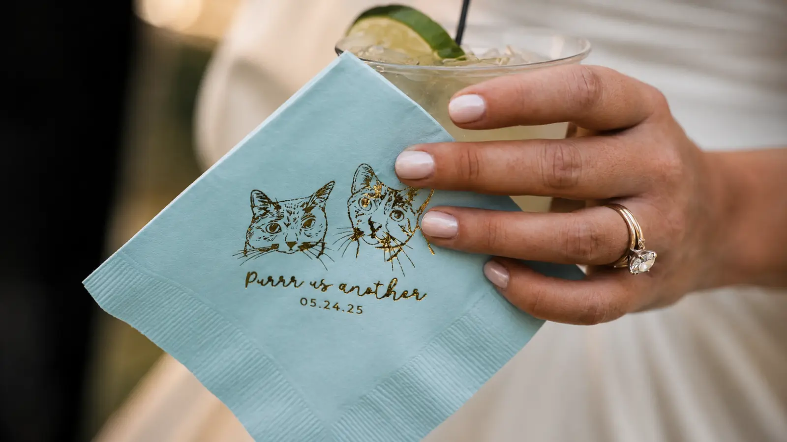 Bride holding a personalized cocktail napkin printed with custom cat portraits while enjoying a signature wedding drink Ways to Honor Your Pet at Your Wedding
