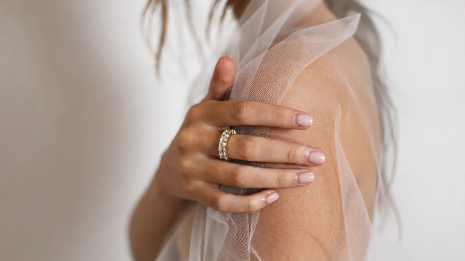 Bride wearing a diamond eternity wedding band while holding a soft tulle veil over her shoulder