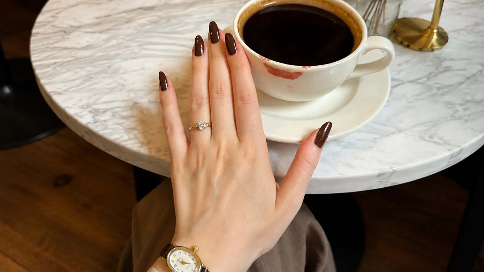 Woman wearing a delicate diamond ring while holding a cup of coffee at a café table