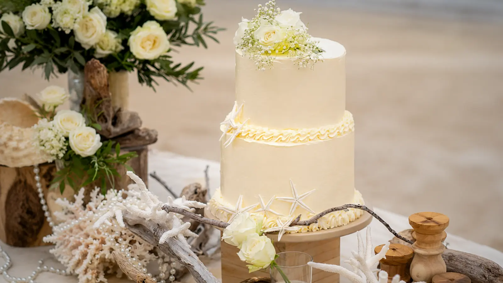 Elegant two-tier beach wedding cake with white frosting, starfish accents, white flowers, coral decorations, and coastal wedding table styling.