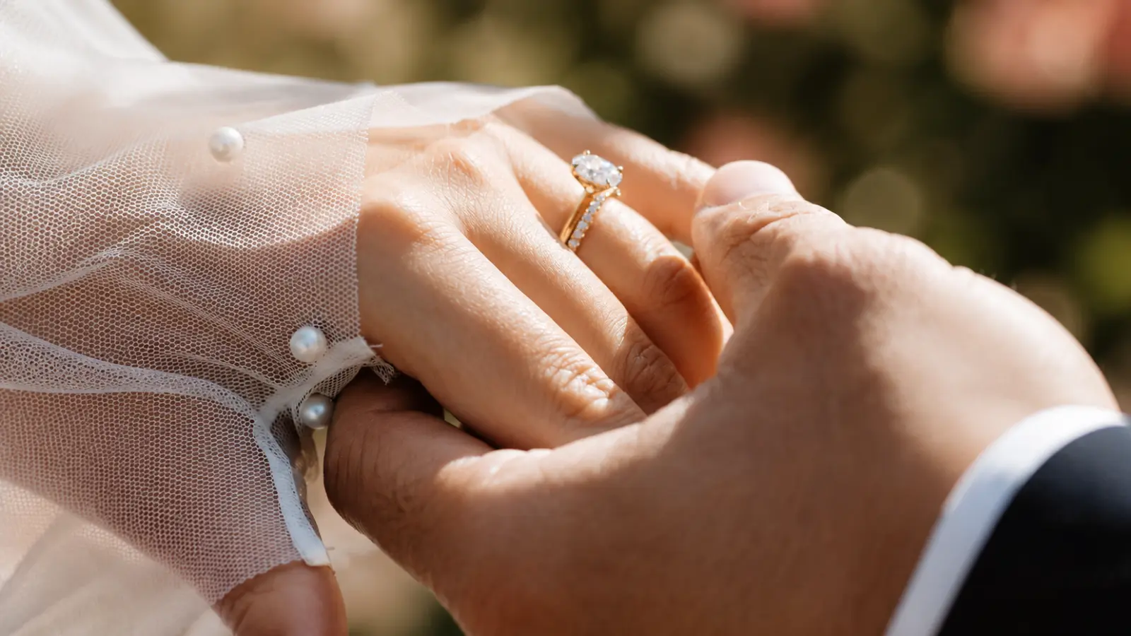 Bride and groom holding hands with an engagement ring and wedding ring, showing the difference between engagement rings and wedding rings.