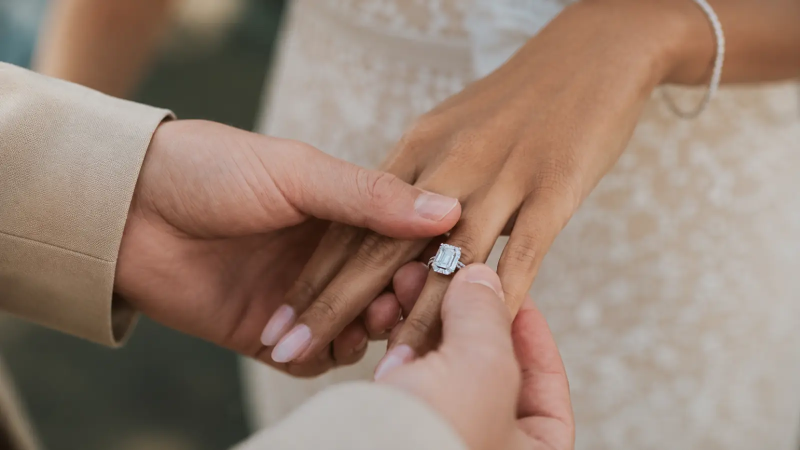 Close-up of a ring being placed on a bride’s hand, showing how engagement rings and wedding rings are traditionally worn.