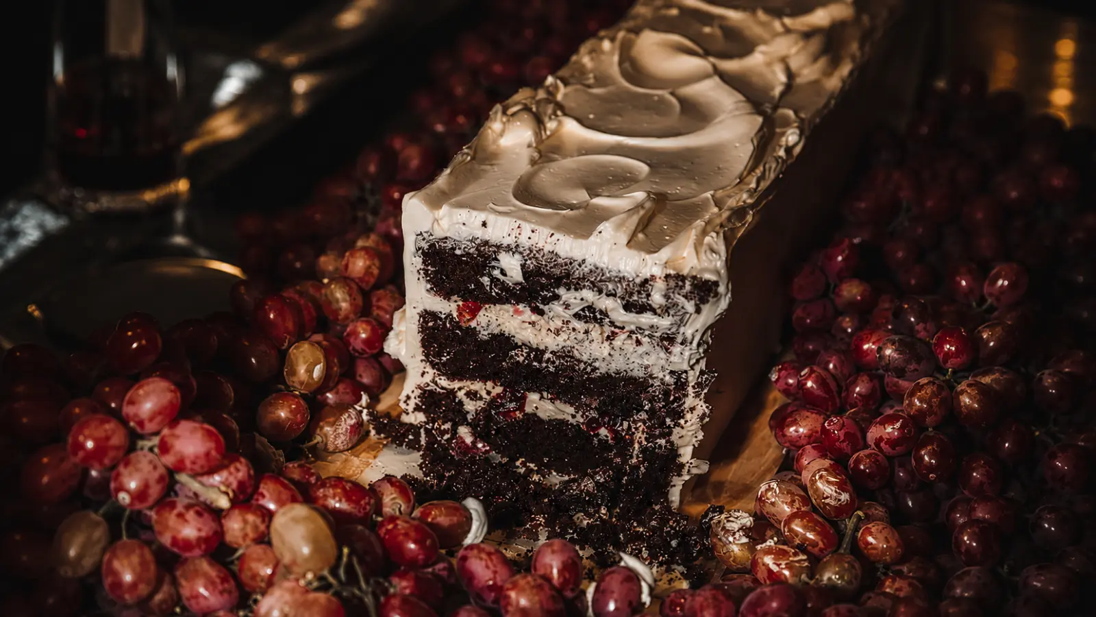 Close-up of a fall wedding cake slice with chocolate layers, cream filling, grapes, and rich seasonal flavors displayed in an elegant setting.