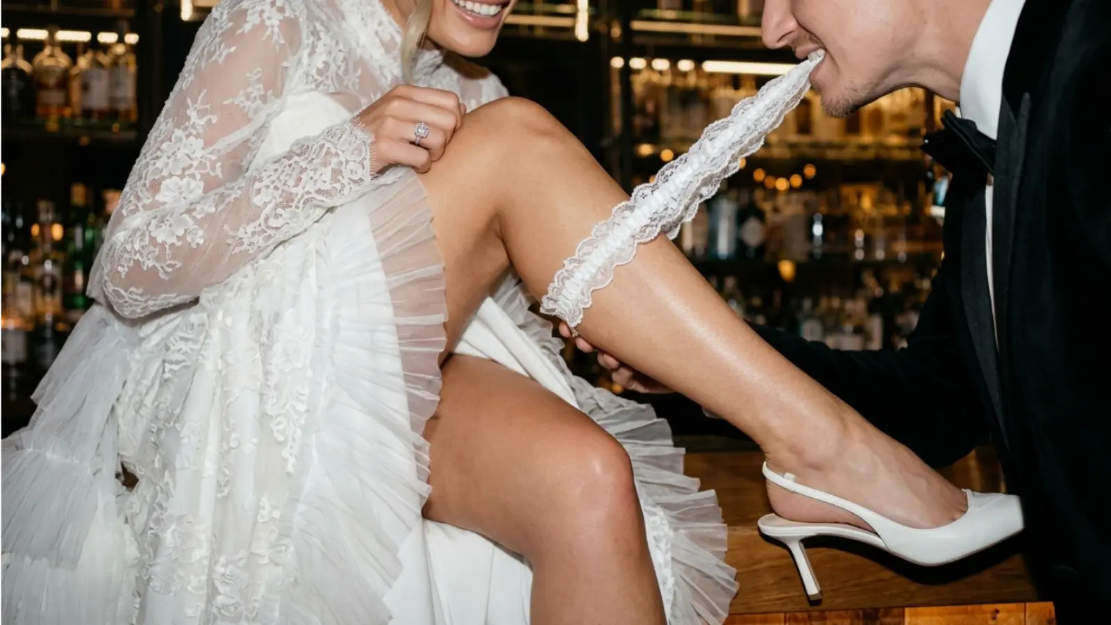 Bride laughing while the groom removes her wedding garter removal during the reception tradition