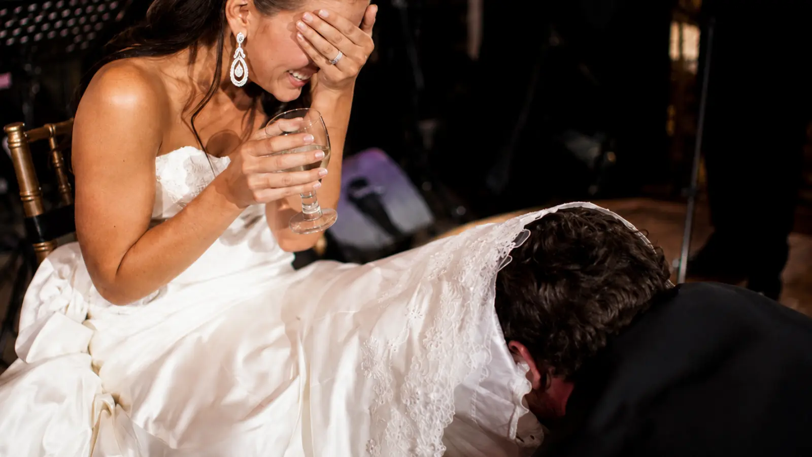 Bride laughing while the groom performs the traditional wedding garter tradition removal during the reception
