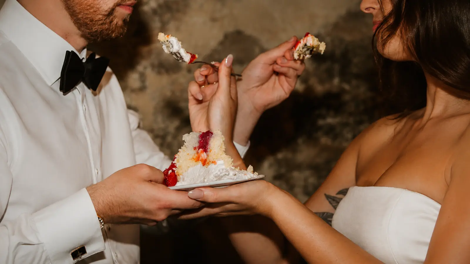 Bride and groom eating wedding cake together after the cake cutting ceremony in a romantic wedding reception setting.