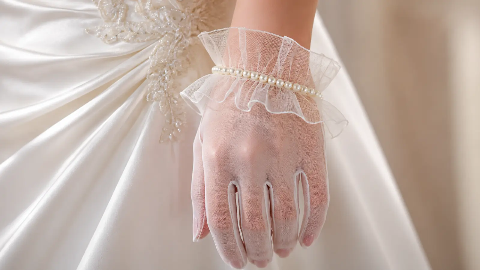 Close-up of pearl embellished tulle wedding gloves on a bride, highlighting a soft and modern wedding glove style