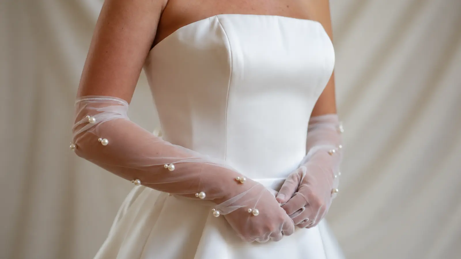 Close-up of sheer pearl bridal gloves styled with a wedding dress, featuring a soft and modern wedding accessory combination