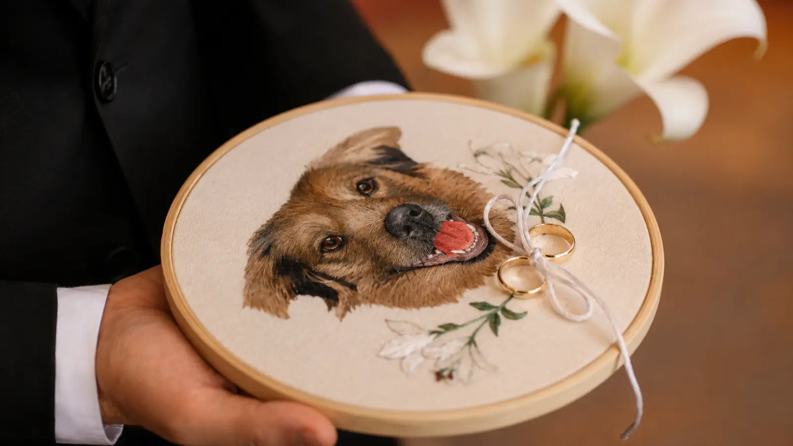 Wedding rings tied to an embroidered hoop with a custom dog portrait, held during the ceremony as a meaningful tribute to a beloved pet