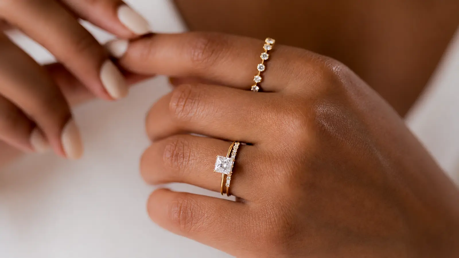 Close-up of a princess-cut diamond engagement ring stacked with a slim diamond wedding band on a woman's hand