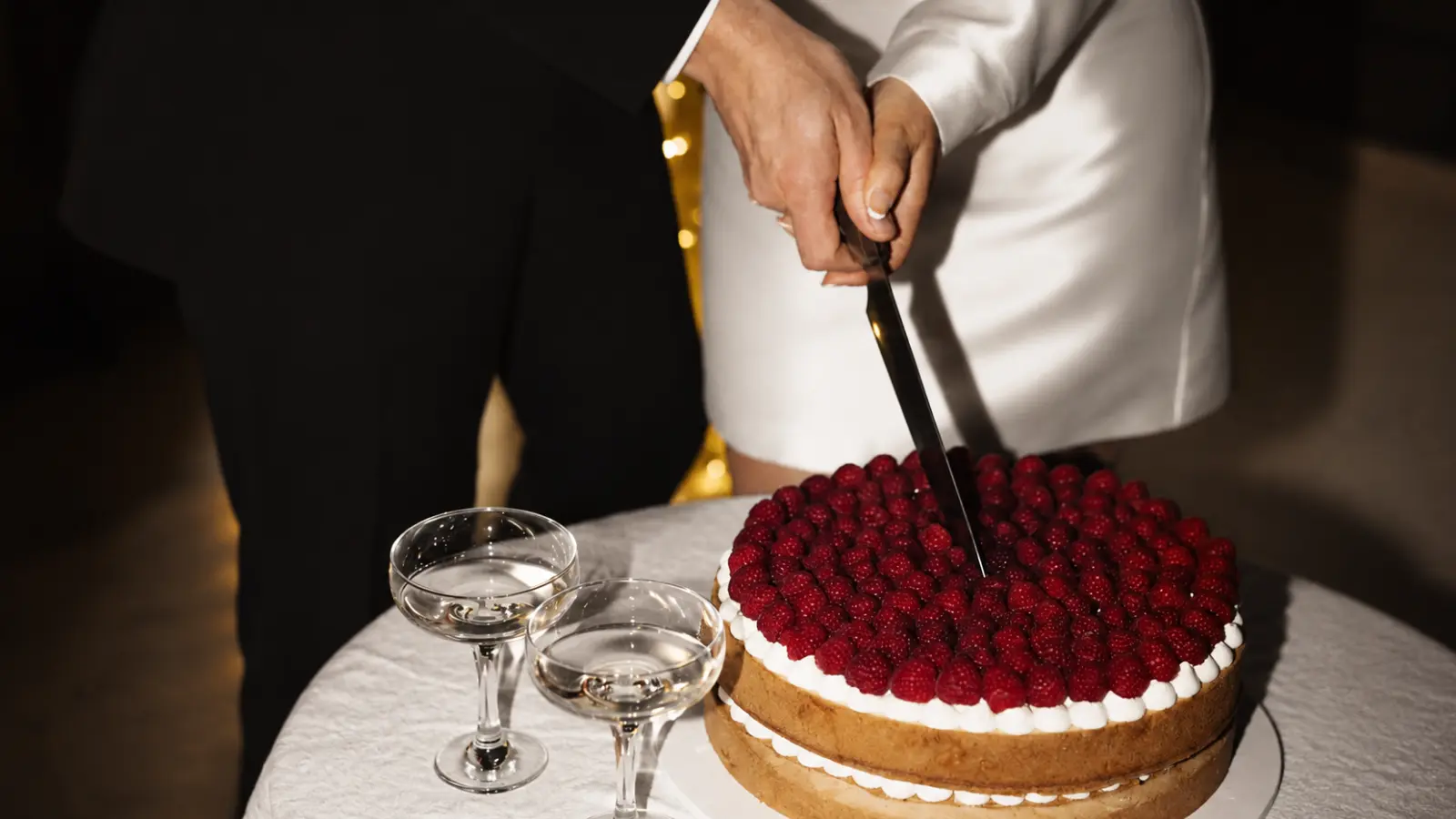 Bride and groom cutting a modern raspberry wedding cake together during their wedding reception cake cutting moment.