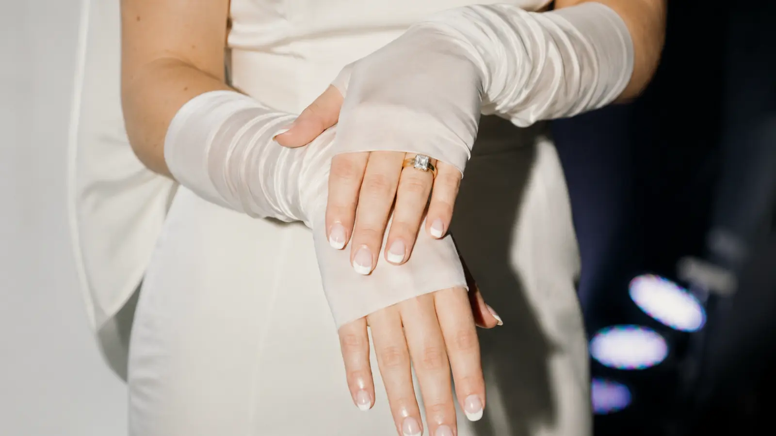 Close-up of satin fingerless wedding gloves with a visible ring, highlighting a classic bridal accessory combination