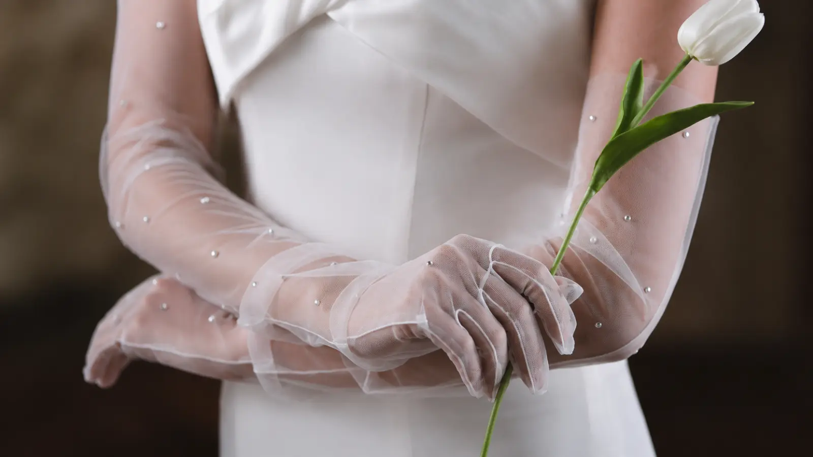 Close-up of sheer long bridal gloves with a flower and wedding dress, highlighting a delicate romantic accessory look