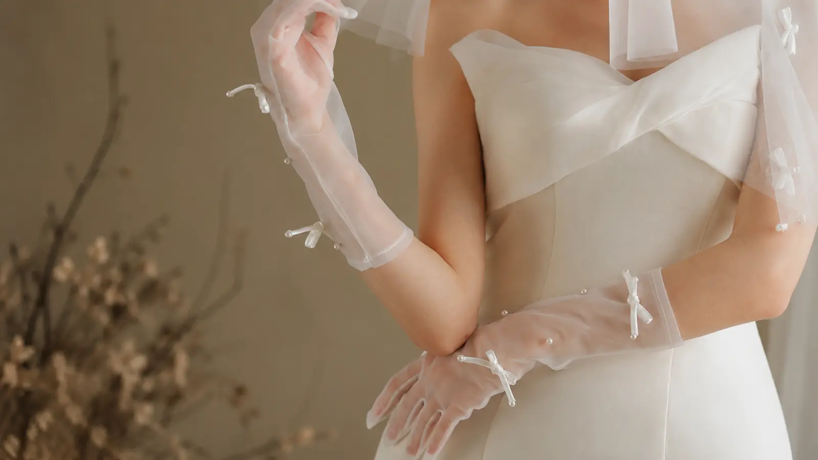 Modern bride wearing sheer wedding gloves with a white dress, featuring delicate pearl details and contemporary bridal styling