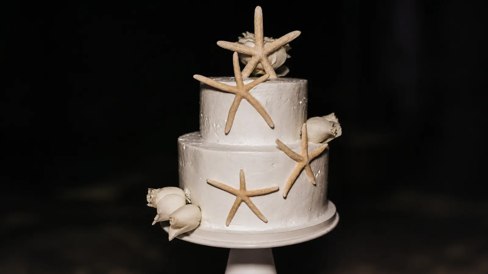 Simple two-tier beach wedding cake with white frosting, starfish decorations, and minimalist ocean-inspired details for a coastal wedding.