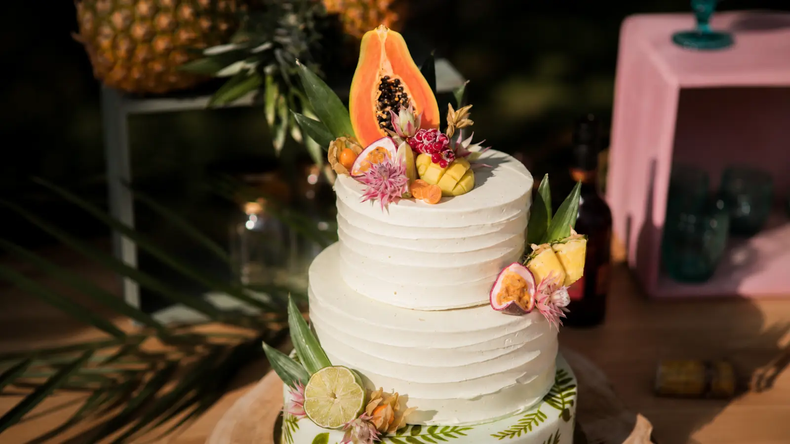 Tropical beach wedding cake with pineapple, papaya, passion fruit, citrus details, tropical leaves, and fresh fruit decorations for an island wedding theme.