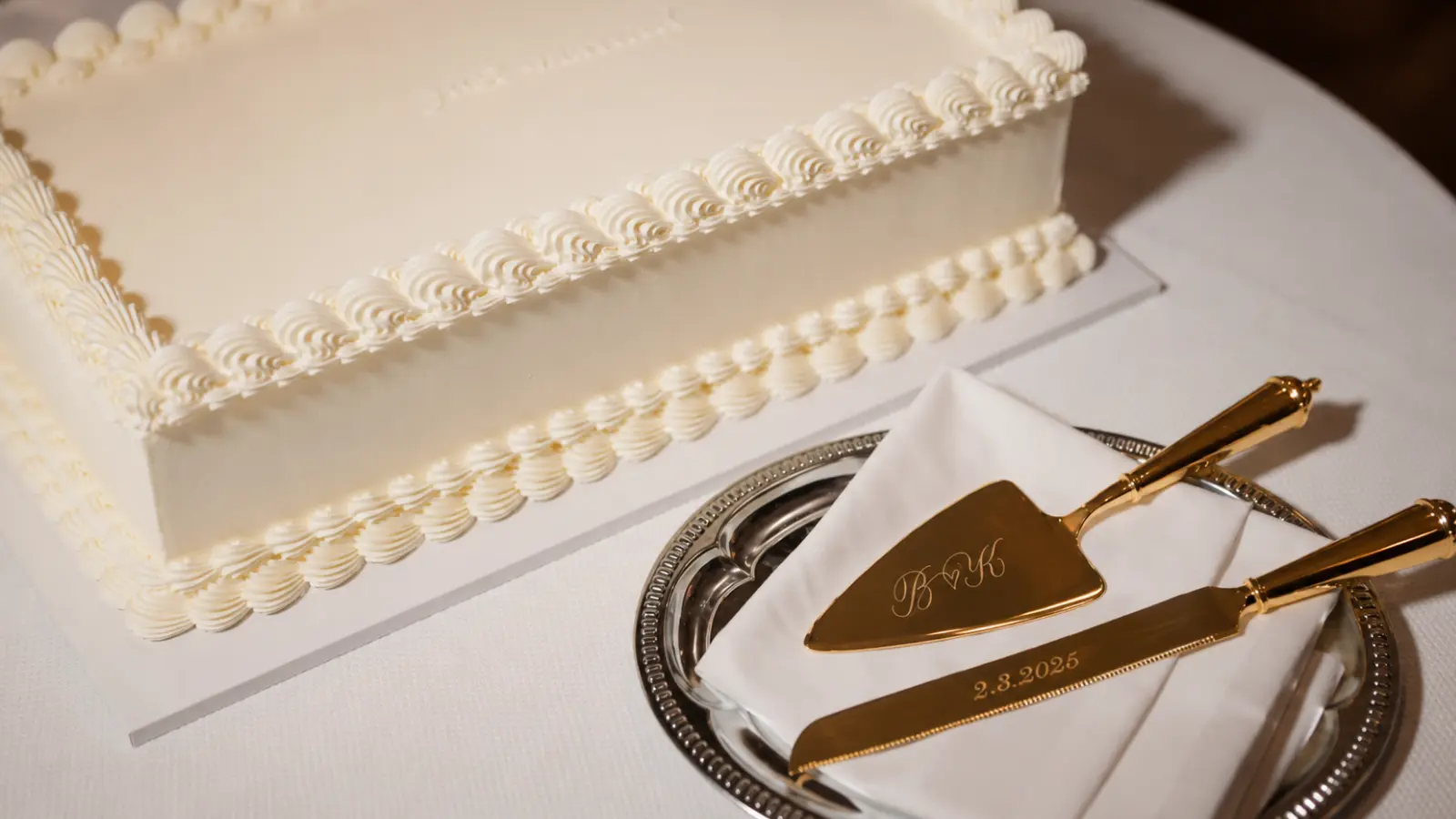 Elegant gold wedding cake knife and serving set placed beside a classic white wedding cake before the cake cutting tradition.