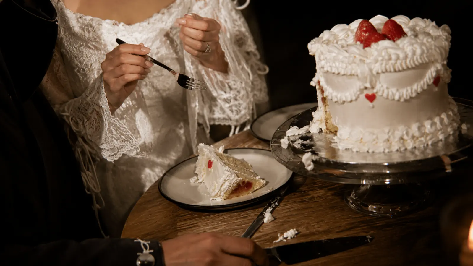 Newlyweds serving and tasting wedding cake together at the reception table after the traditional wedding cake cutting.