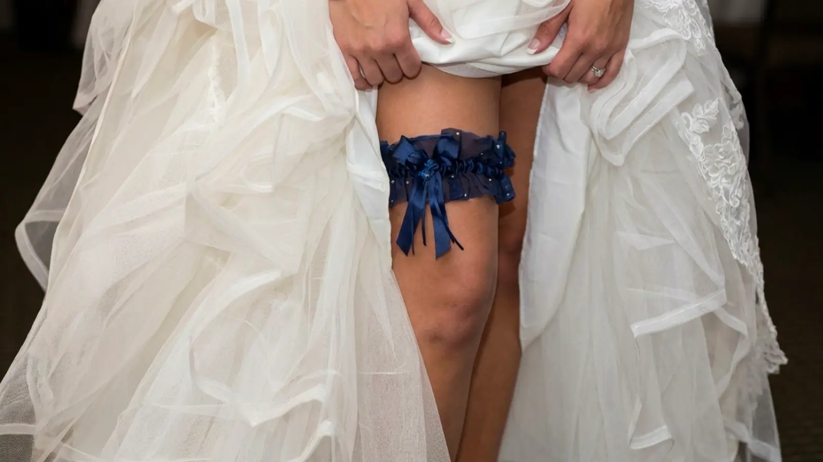 Bride lifting her wedding dress to show a blue wedding garter correctly positioned on her upper thigh
