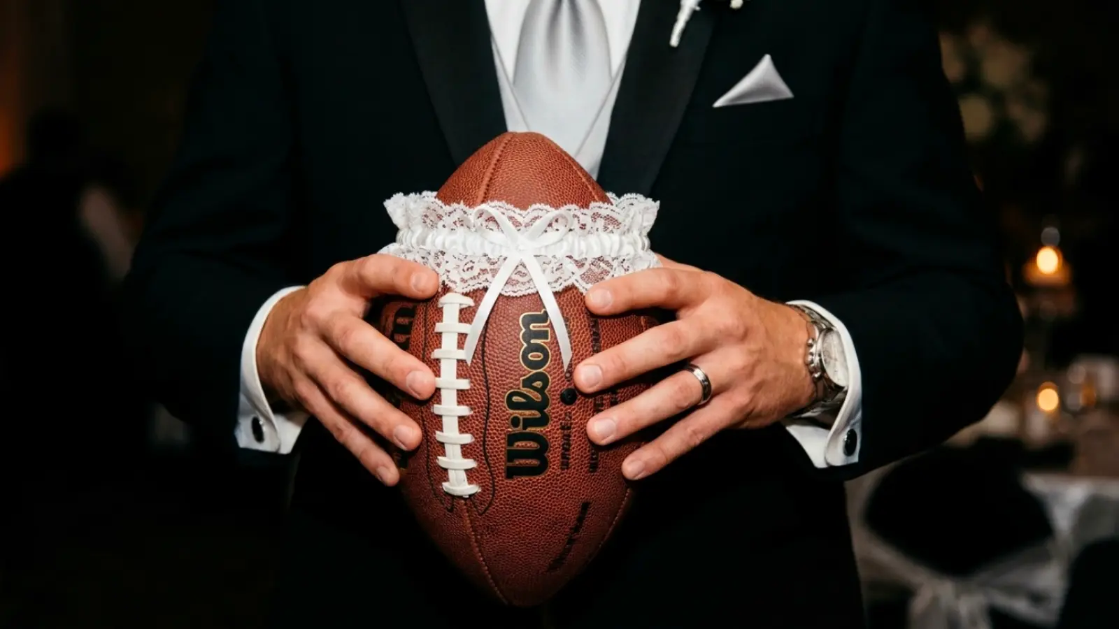 Groom holding a football decorated with a wedding garter as a modern garter toss alternative