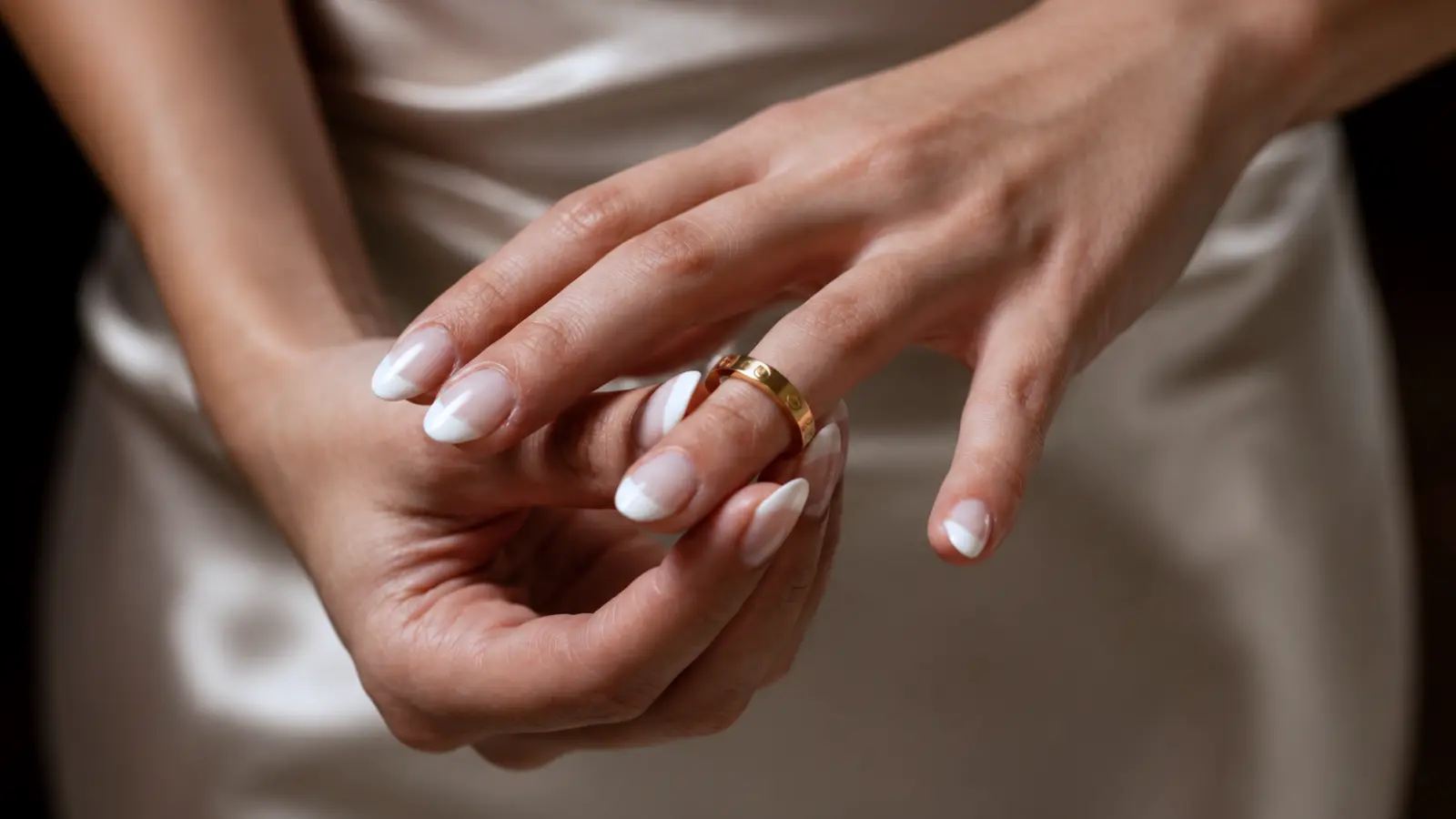 Close-up of a woman wearing a classic polished yellow gold wedding band with elegant French manicure