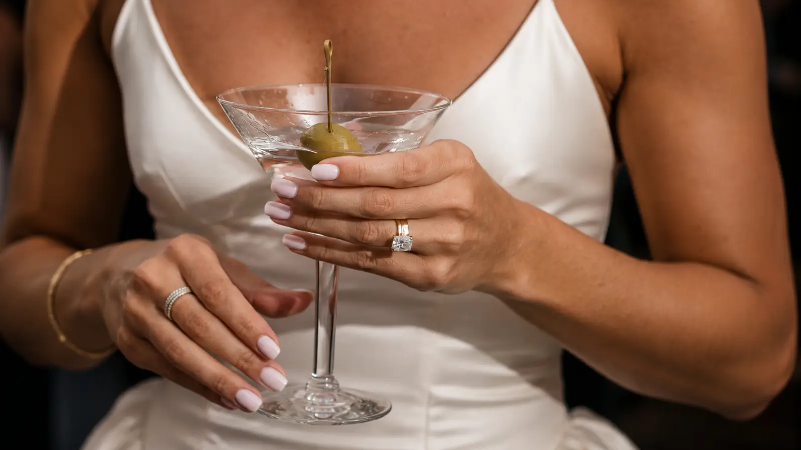Bride holding a cocktail glass while wearing a classic engagement ring paired with a simple wedding band for everyday elegance