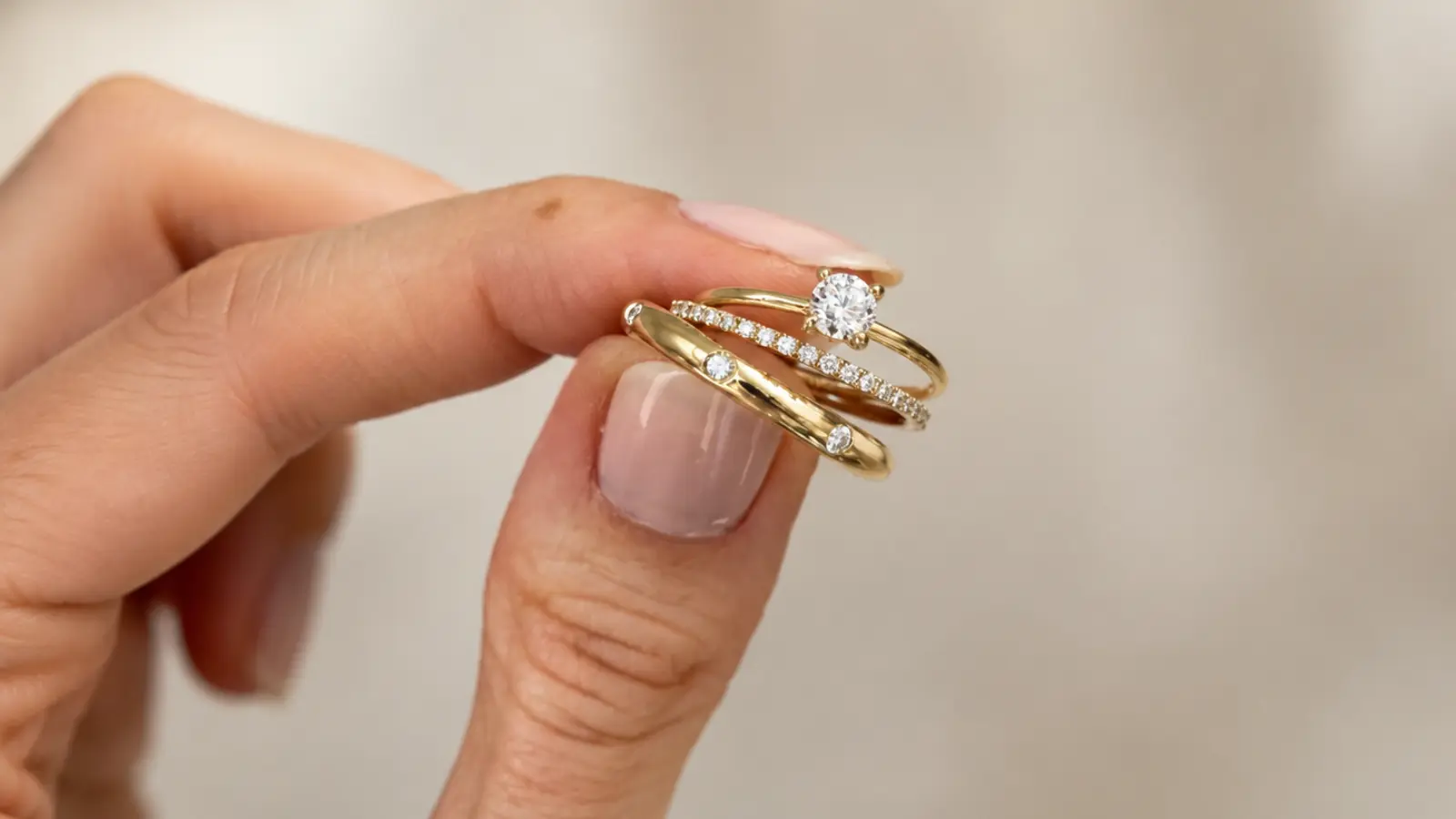 Close-up of a woman's hand holding a stacked yellow gold engagement ring and wedding band set with diamond accents wedding rings for women