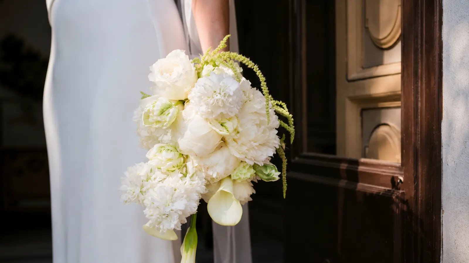 Bride holding an all white wedding bouquets with peonies, calla lilies and trailing greenery