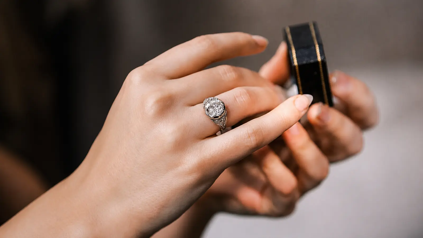 A woman holding an antique diamond engagement ring while opening a ring box during a jewelry shopping experience