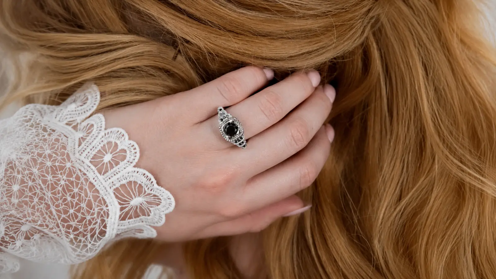 A hand wearing an antique gothic black halo ring with intricate vintage detailing and a black center stone
