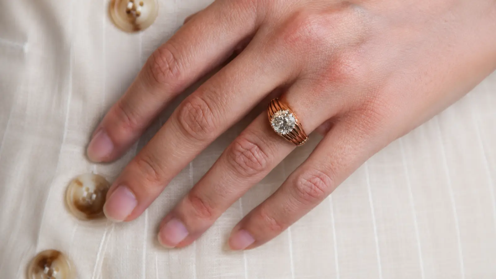 A hand wearing an Art Deco solitaire engagement ring with a ribbed yellow gold band and a classic round diamond centerpiece