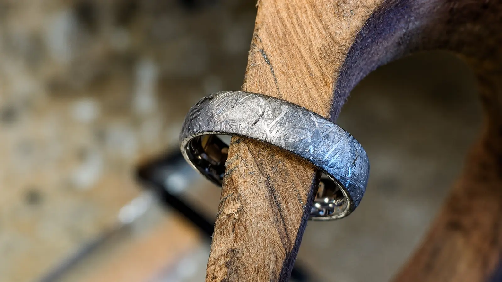 An authentic meteorite wedding ring is displayed on a wooden branch, showcasing the naturally formed crystalline pattern unique to genuine meteorite wedding bands