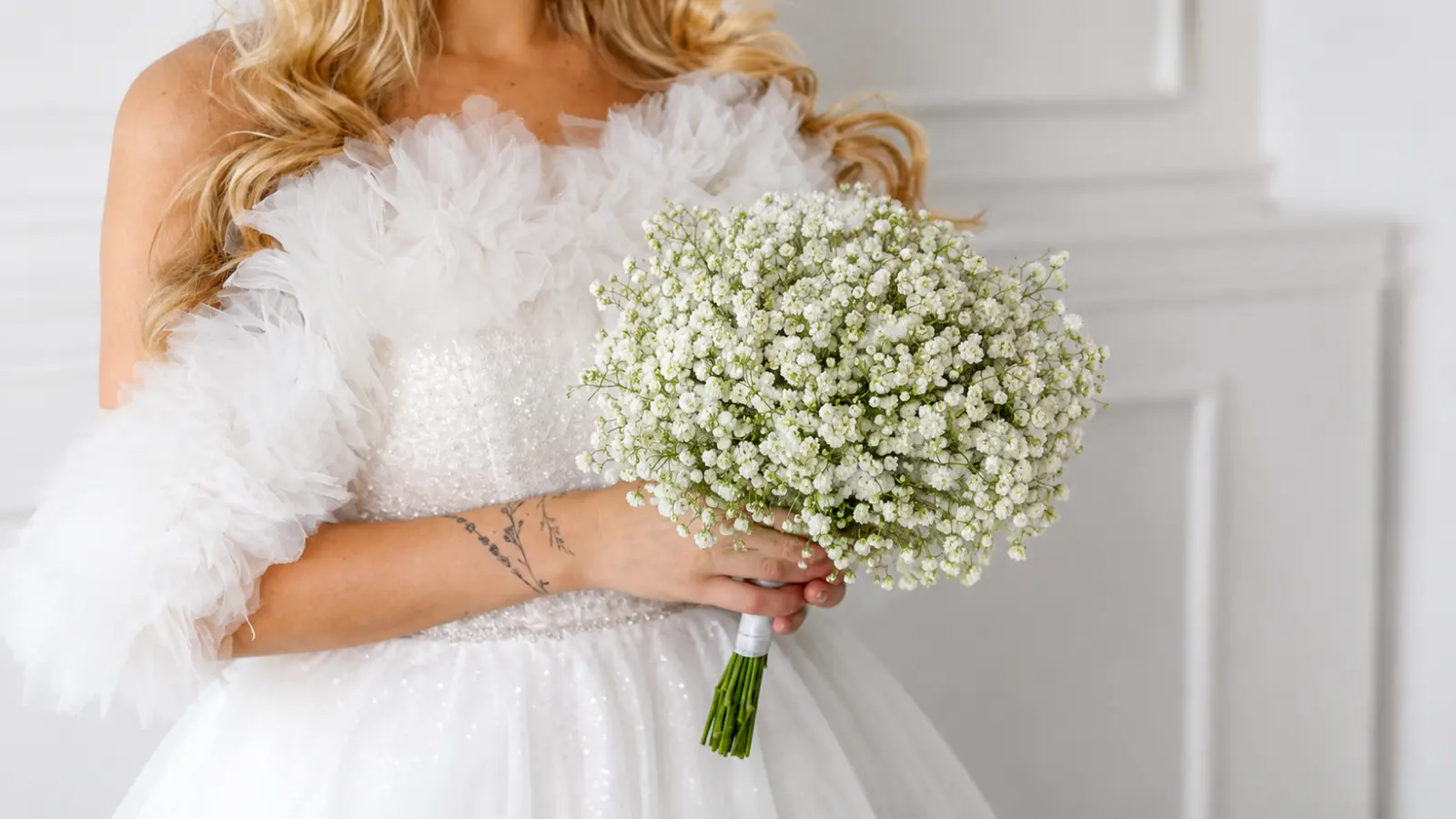 Bride holding a round baby's breath wedding bouquet with delicate white blooms and a modern bridal gown