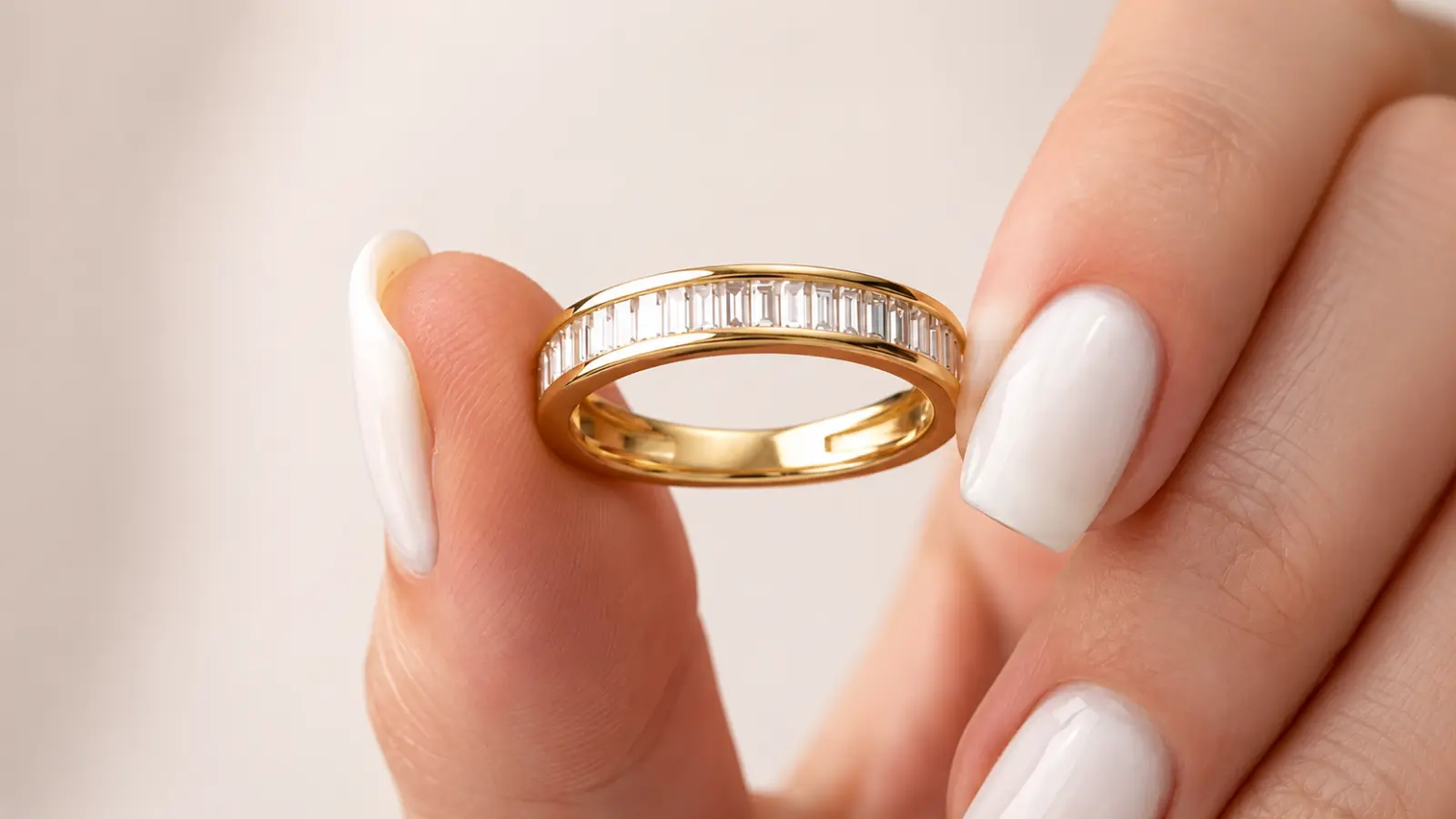 A baguette diamond eternity wedding band held between two fingers for a close-up view
