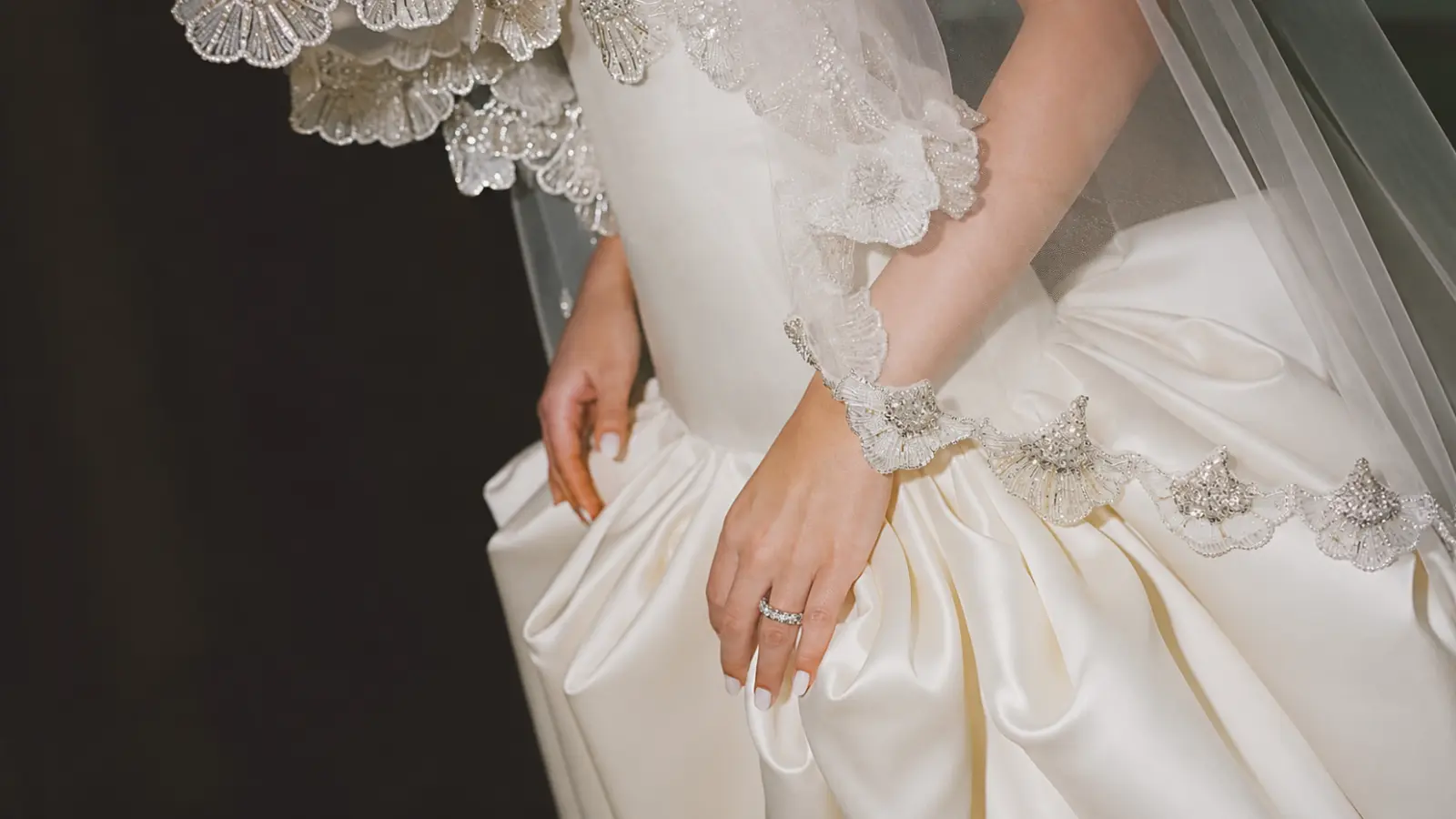 Bride wearing a satin wedding dress with a beaded edge veil that coordinates perfectly with the gown's elegant detailing