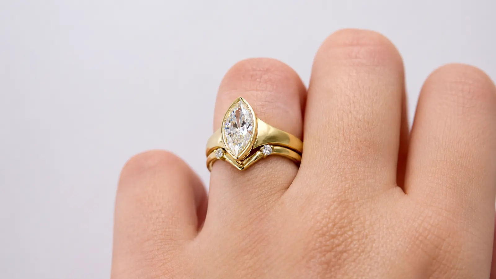 A bezel set marquise engagement ring paired with a contour gold wedding band on a woman's hand