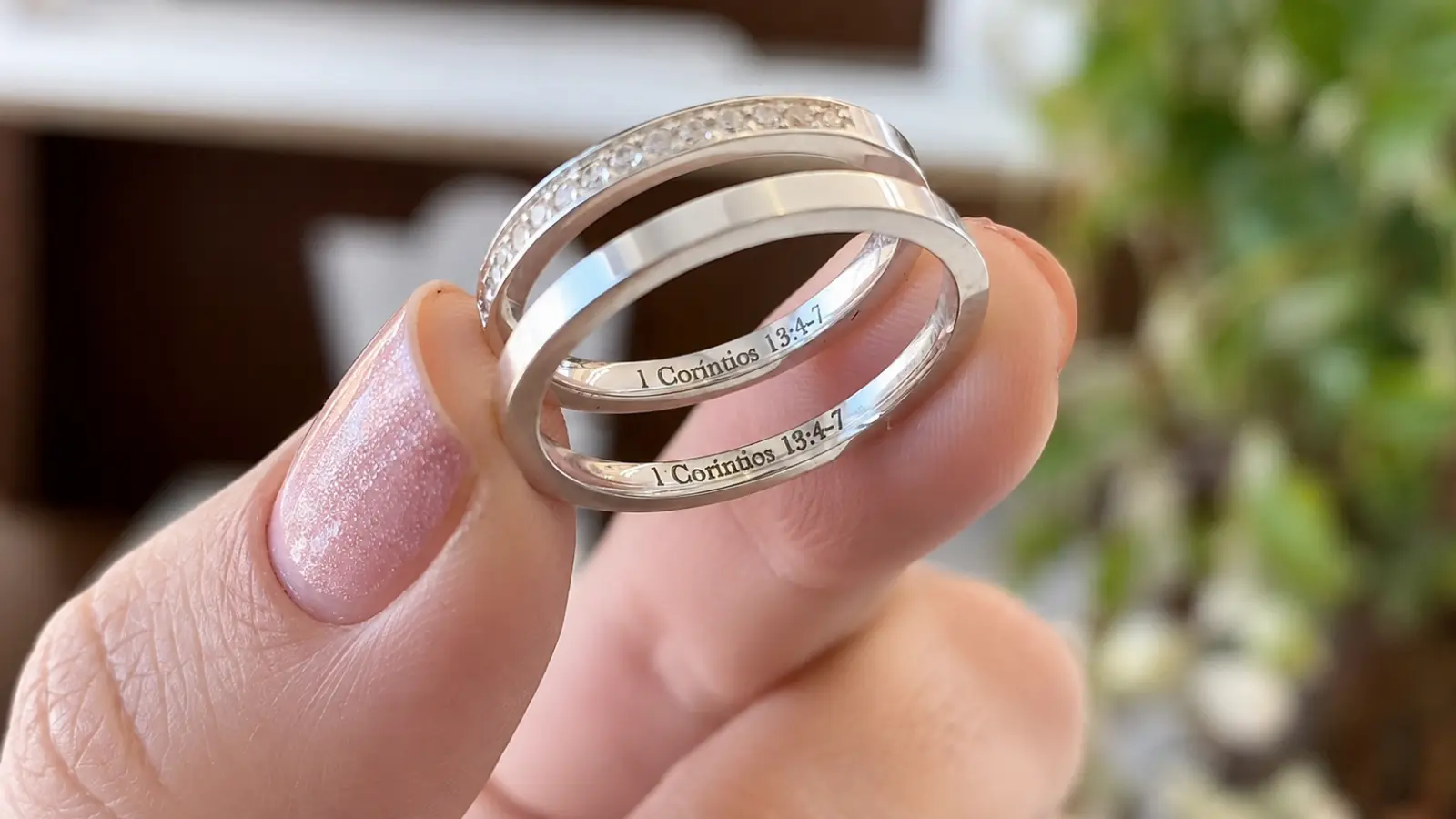 Two wedding rings engraved with a Bible verse inside the bands held between a person's fingers