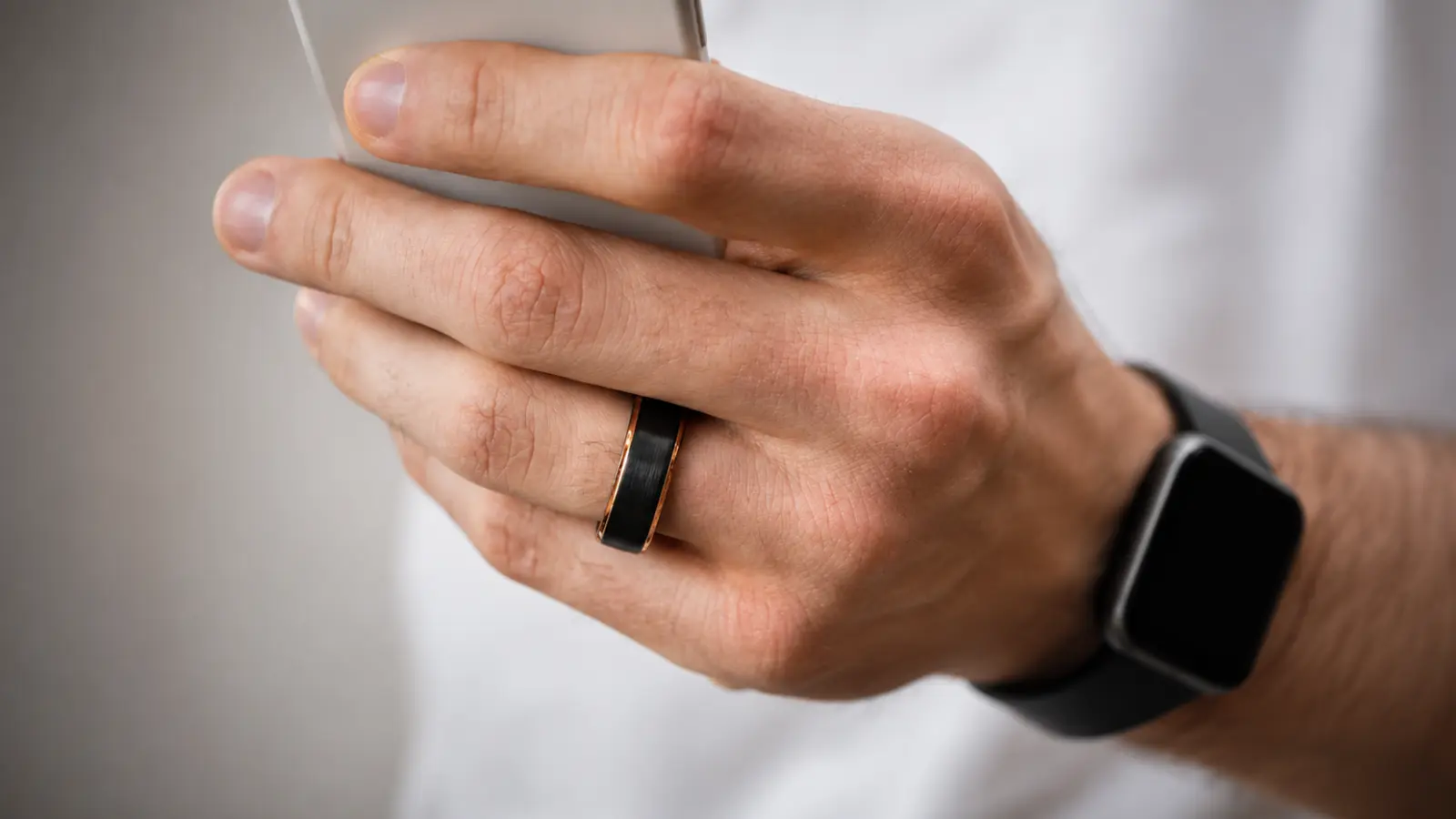 A man holding a smartphone while wearing a black and gold wedding band with a modern two-tone finish