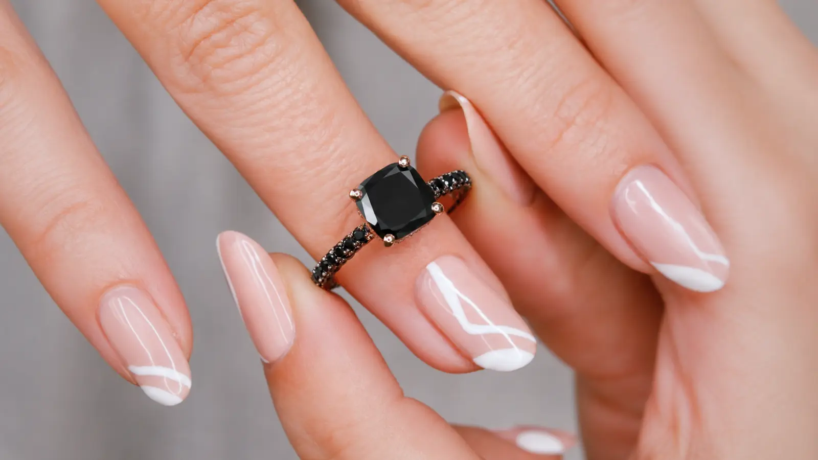 A close-up of a black cushion cut wedding ring with a pavé black diamond band and elegant manicure Black Wedding Rings